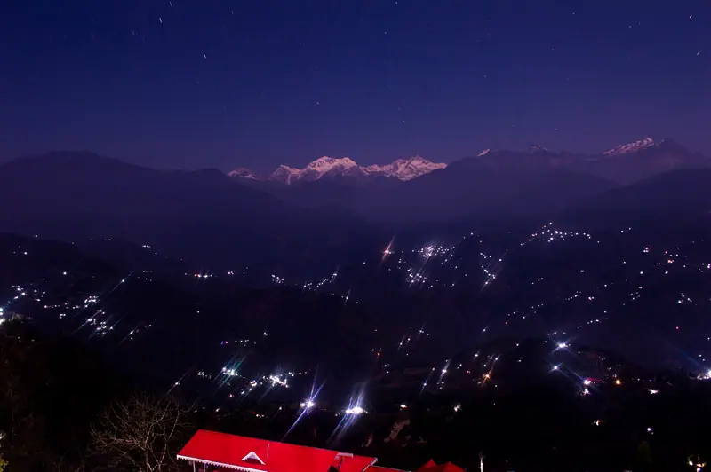 The Kanchenjunga massif glowing at dusk above the lights of a hill town